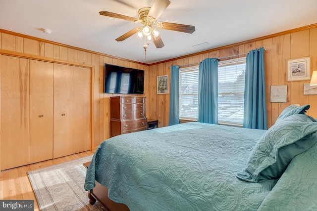 bedroom with wooden walls, ceiling fan, light hardwood / wood-style floors, crown molding, and a closet