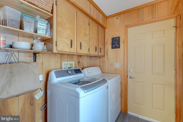 clothes washing area with cabinets, crown molding, washer and dryer, and wood walls