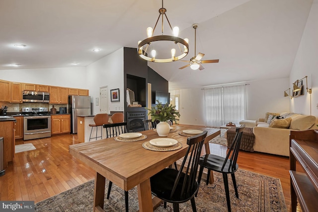 dining space featuring high vaulted ceiling, ceiling fan with notable chandelier, and light wood-type flooring