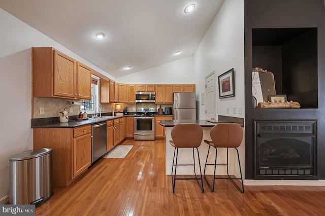 kitchen with sink, stainless steel appliances, a kitchen breakfast bar, decorative backsplash, and light wood-type flooring