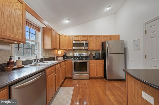 kitchen with lofted ceiling, sink, tasteful backsplash, light hardwood / wood-style flooring, and appliances with stainless steel finishes