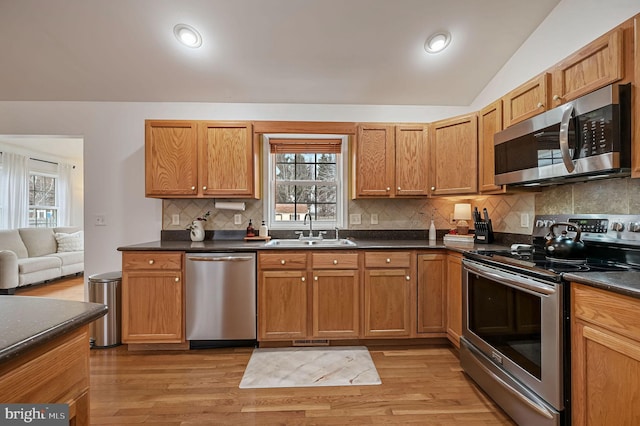 kitchen featuring lofted ceiling, sink, stainless steel appliances, decorative backsplash, and light wood-type flooring