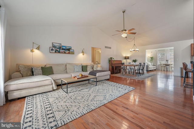 living room featuring hardwood / wood-style flooring, ceiling fan with notable chandelier, and high vaulted ceiling