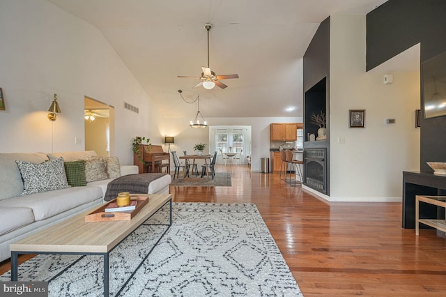 living room featuring high vaulted ceiling, wood-type flooring, and ceiling fan with notable chandelier