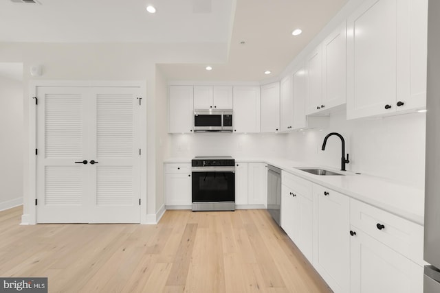 kitchen featuring sink, white cabinetry, light wood-type flooring, decorative backsplash, and appliances with stainless steel finishes