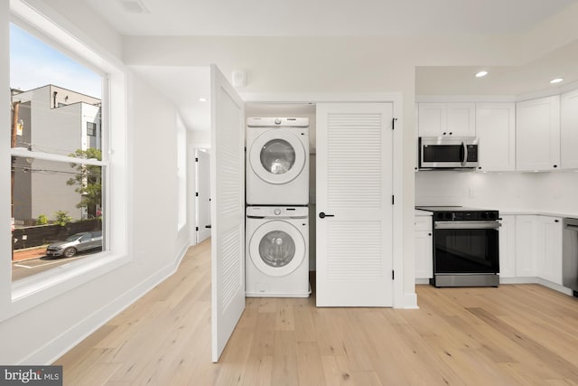 laundry area with light hardwood / wood-style flooring and stacked washer / drying machine