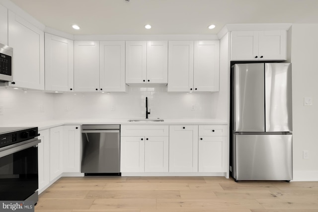 kitchen with white cabinets, stainless steel appliances, light wood-type flooring, sink, and backsplash