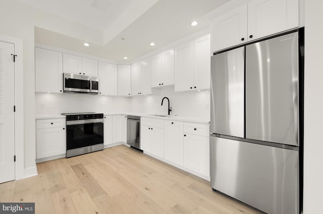 kitchen featuring appliances with stainless steel finishes, light hardwood / wood-style floors, white cabinetry, and sink