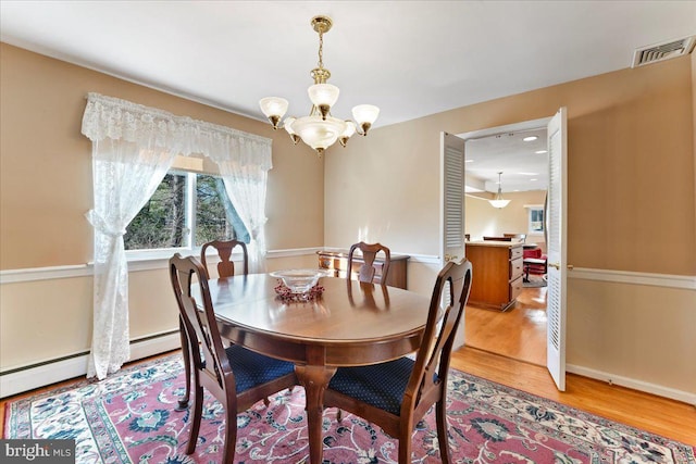 dining space featuring a baseboard heating unit, an inviting chandelier, and light wood-type flooring