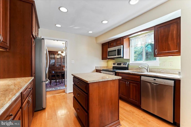 kitchen with appliances with stainless steel finishes, a center island, a notable chandelier, sink, and light hardwood / wood-style flooring