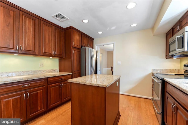 kitchen featuring stainless steel appliances, light wood-type flooring, light stone counters, and a kitchen island