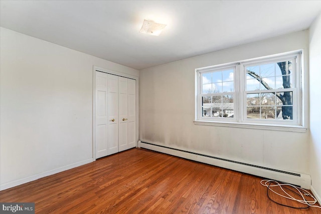 unfurnished bedroom featuring a closet, wood-type flooring, and a baseboard heating unit