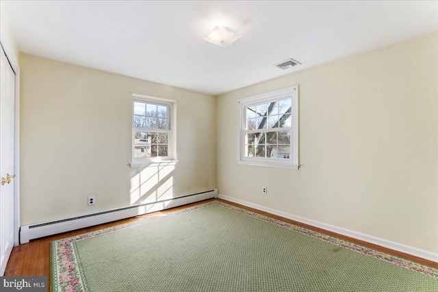 unfurnished room with baseboard heating, a healthy amount of sunlight, and hardwood / wood-style floors