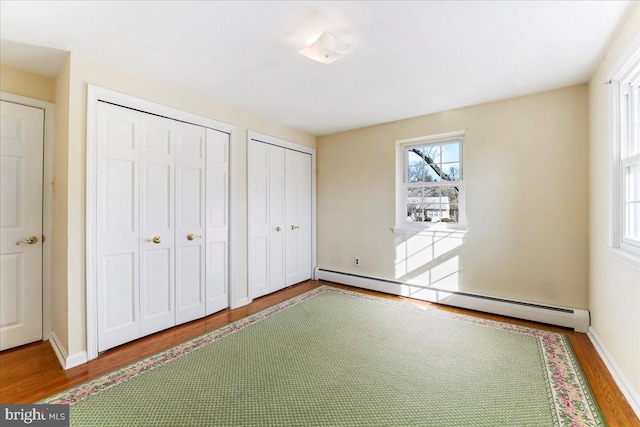 unfurnished bedroom with multiple closets, hardwood / wood-style flooring, and a baseboard heating unit