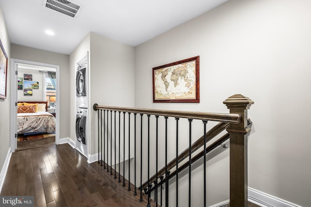 corridor with stacked washer / drying machine and dark hardwood / wood-style floors