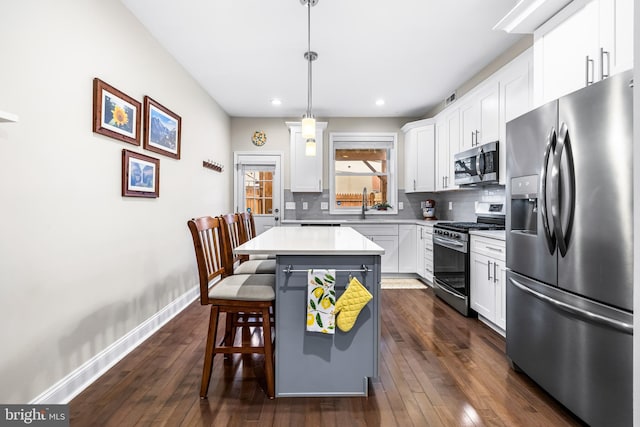 kitchen with decorative light fixtures, a kitchen island, decorative backsplash, white cabinetry, and stainless steel appliances