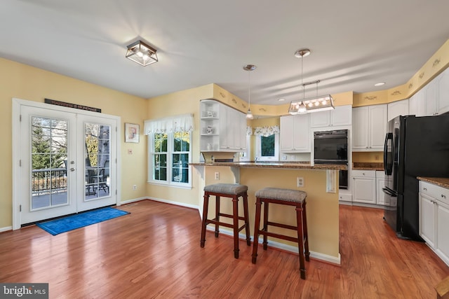 kitchen with pendant lighting, black appliances, white cabinetry, a healthy amount of sunlight, and a kitchen breakfast bar