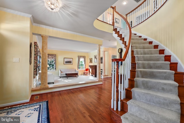 foyer entrance featuring ornamental molding, ornate columns, a notable chandelier, and hardwood / wood-style floors