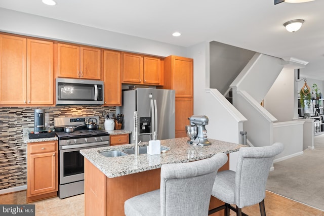 kitchen featuring light stone countertops, a center island with sink, a kitchen bar, decorative backsplash, and stainless steel appliances