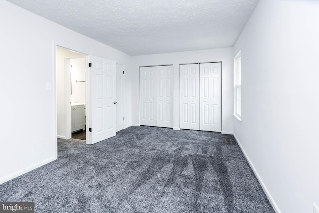 unfurnished bedroom with a textured ceiling, dark colored carpet, and two closets