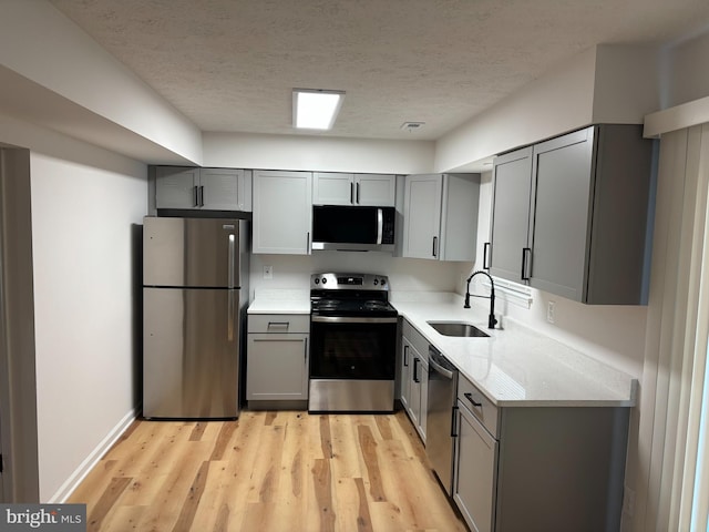 kitchen with a textured ceiling, appliances with stainless steel finishes, sink, gray cabinets, and light stone counters