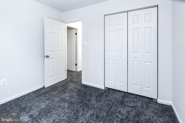 unfurnished bedroom featuring dark carpet, a closet, and a textured ceiling