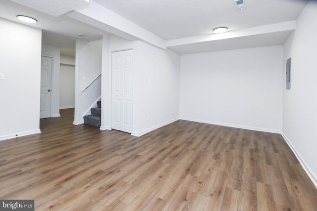 basement with a textured ceiling, electric panel, and dark hardwood / wood-style floors