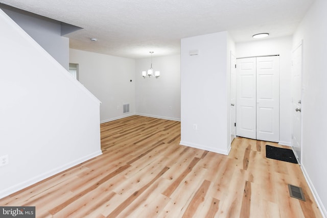 spare room featuring a textured ceiling, a chandelier, and light hardwood / wood-style floors