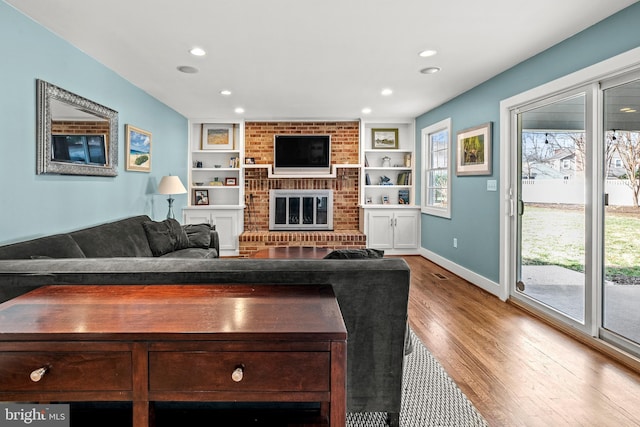 living room featuring built in shelves, a brick fireplace, and hardwood / wood-style flooring