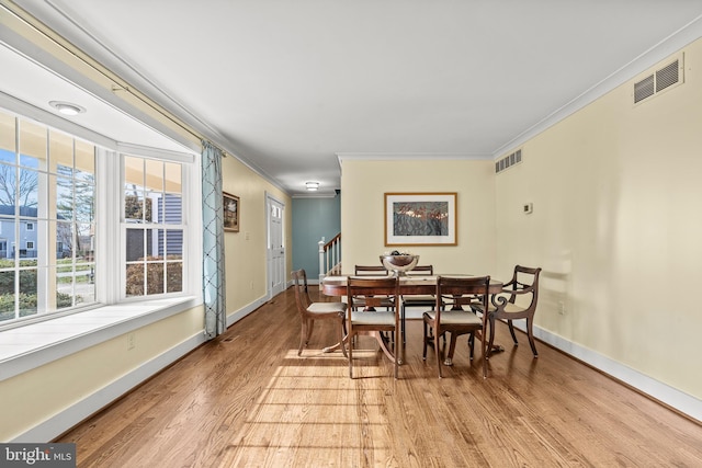 dining space with light hardwood / wood-style floors, ornamental molding, and a healthy amount of sunlight