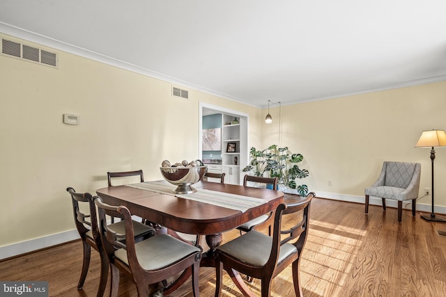 dining room with ornamental molding, hardwood / wood-style floors, and built in shelves