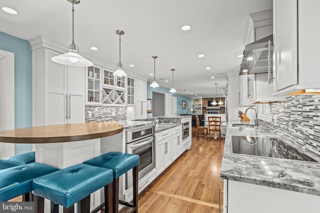 kitchen with oven, white cabinetry, decorative light fixtures, and sink