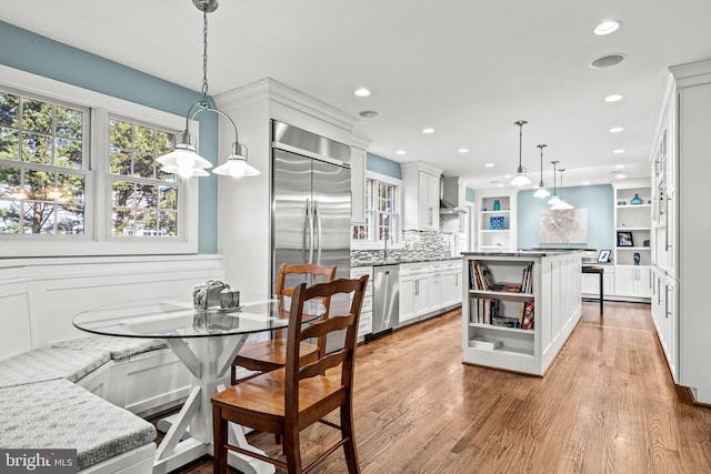 kitchen featuring decorative light fixtures, light hardwood / wood-style floors, a kitchen island, white cabinetry, and appliances with stainless steel finishes