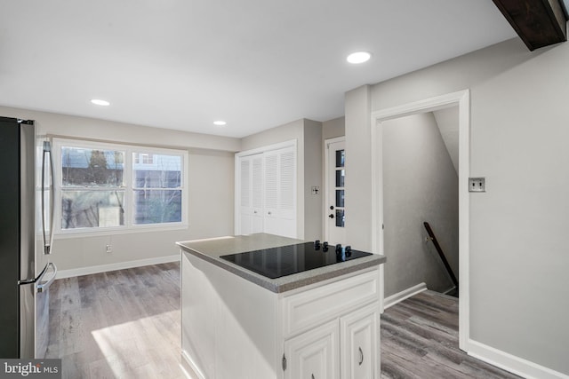 kitchen with black electric stovetop, light hardwood / wood-style floors, white cabinets, and stainless steel fridge