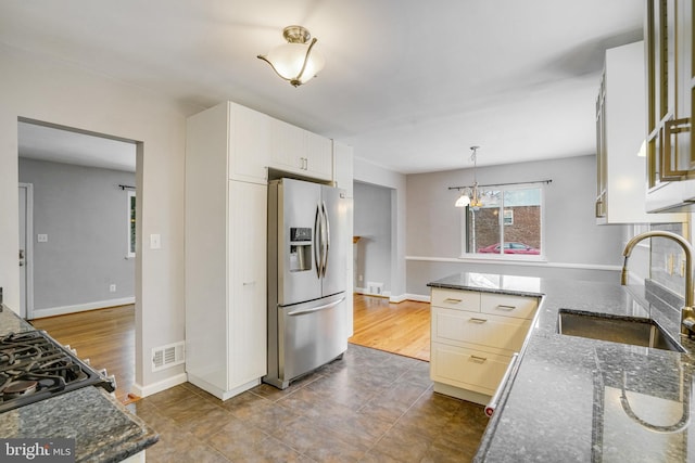 kitchen with sink, stainless steel fridge, hanging light fixtures, white cabinets, and dark stone counters