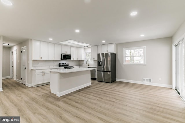 kitchen with appliances with stainless steel finishes, backsplash, white cabinets, light hardwood / wood-style flooring, and a center island