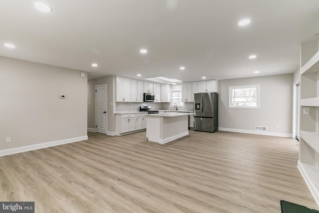 kitchen with backsplash, a center island, white cabinetry, light wood-type flooring, and stainless steel appliances