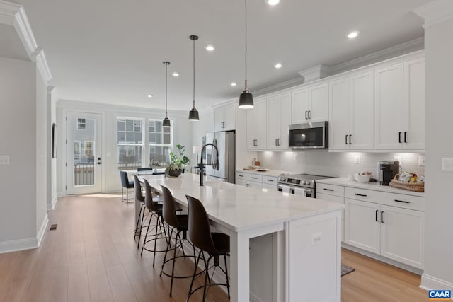 kitchen with appliances with stainless steel finishes, hanging light fixtures, white cabinetry, and a center island with sink