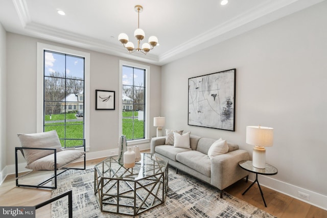 living room featuring a raised ceiling, an inviting chandelier, hardwood / wood-style floors, and ornamental molding