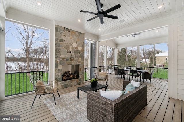 sunroom with ceiling fan, a wealth of natural light, and an outdoor stone fireplace