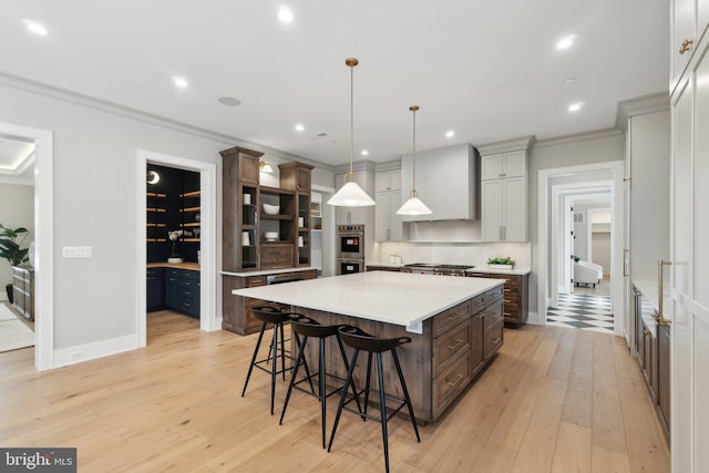 kitchen featuring decorative light fixtures, custom range hood, a kitchen bar, light hardwood / wood-style floors, and a spacious island