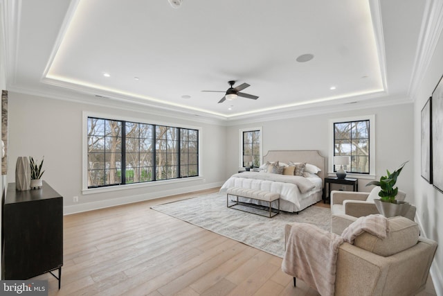 bedroom with ceiling fan, light wood-type flooring, multiple windows, and a tray ceiling