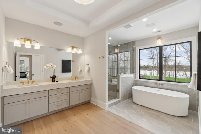 bathroom with hardwood / wood-style floors, a raised ceiling, separate shower and tub, and vanity