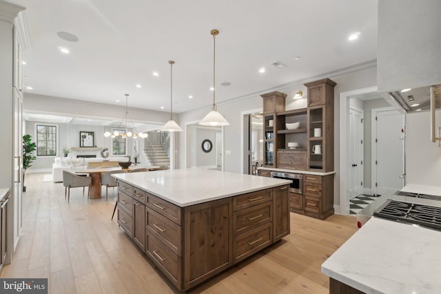 kitchen featuring light wood-type flooring, decorative light fixtures, light stone counters, and a spacious island