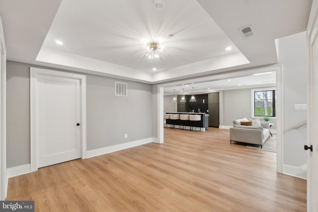 unfurnished living room featuring light wood-type flooring and a tray ceiling