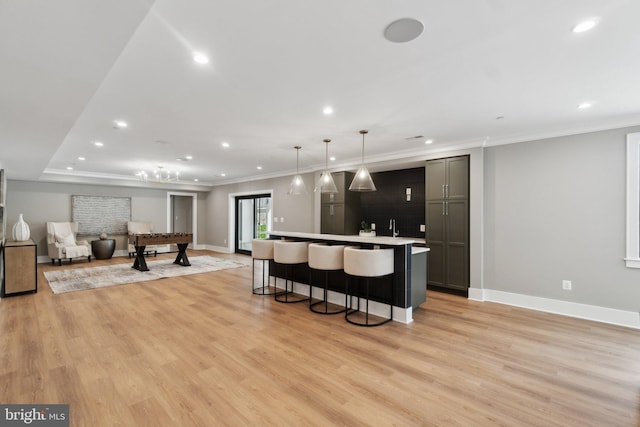 kitchen with a center island with sink, light hardwood / wood-style floors, hanging light fixtures, ornamental molding, and a kitchen bar