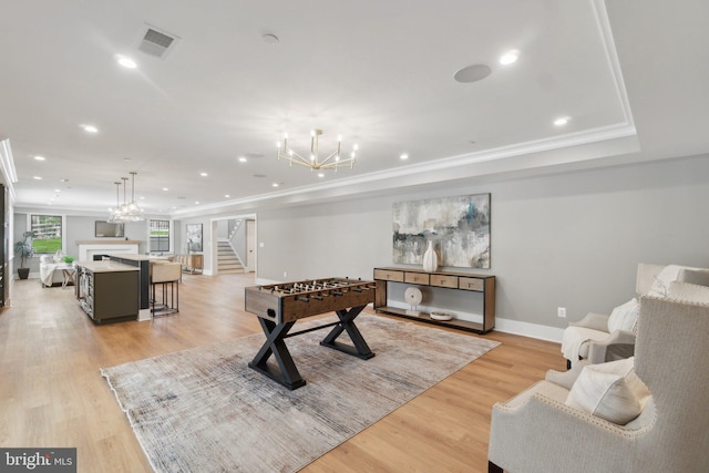 playroom featuring crown molding, a raised ceiling, light hardwood / wood-style flooring, and an inviting chandelier