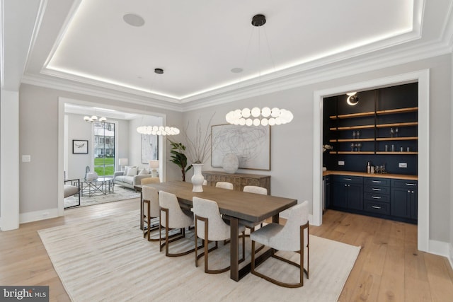 dining room with crown molding, a raised ceiling, a notable chandelier, and light hardwood / wood-style flooring