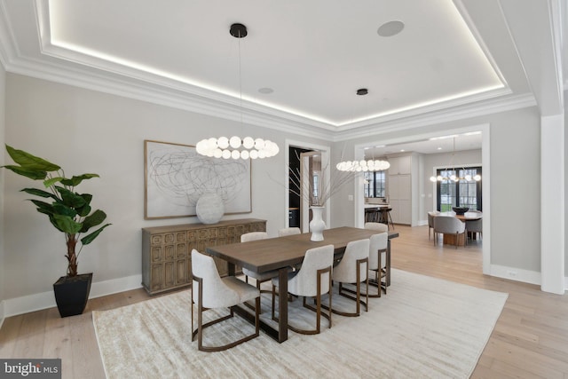 dining area featuring a notable chandelier, light hardwood / wood-style floors, and a tray ceiling