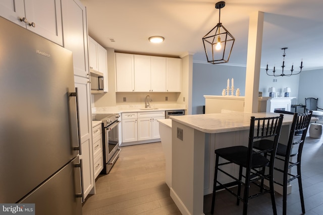 kitchen featuring sink, a breakfast bar area, appliances with stainless steel finishes, white cabinetry, and hanging light fixtures